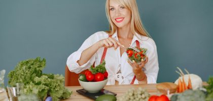 Blonde woman enjoying a fresh salad surrounded by vegetables, promoting healthy eating.